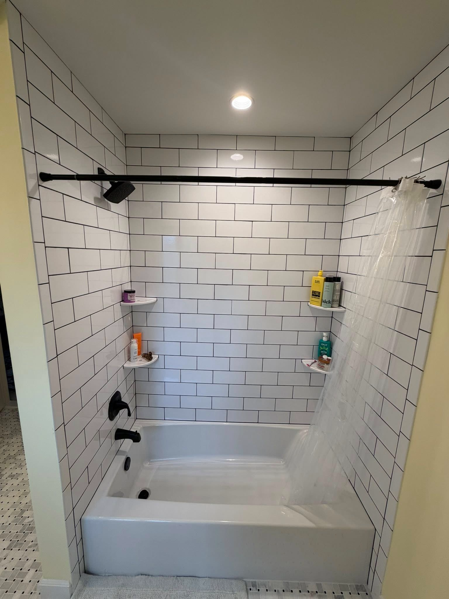 Modern tiled shower stall with built-in bench, black shower rod, and recessed ceiling light