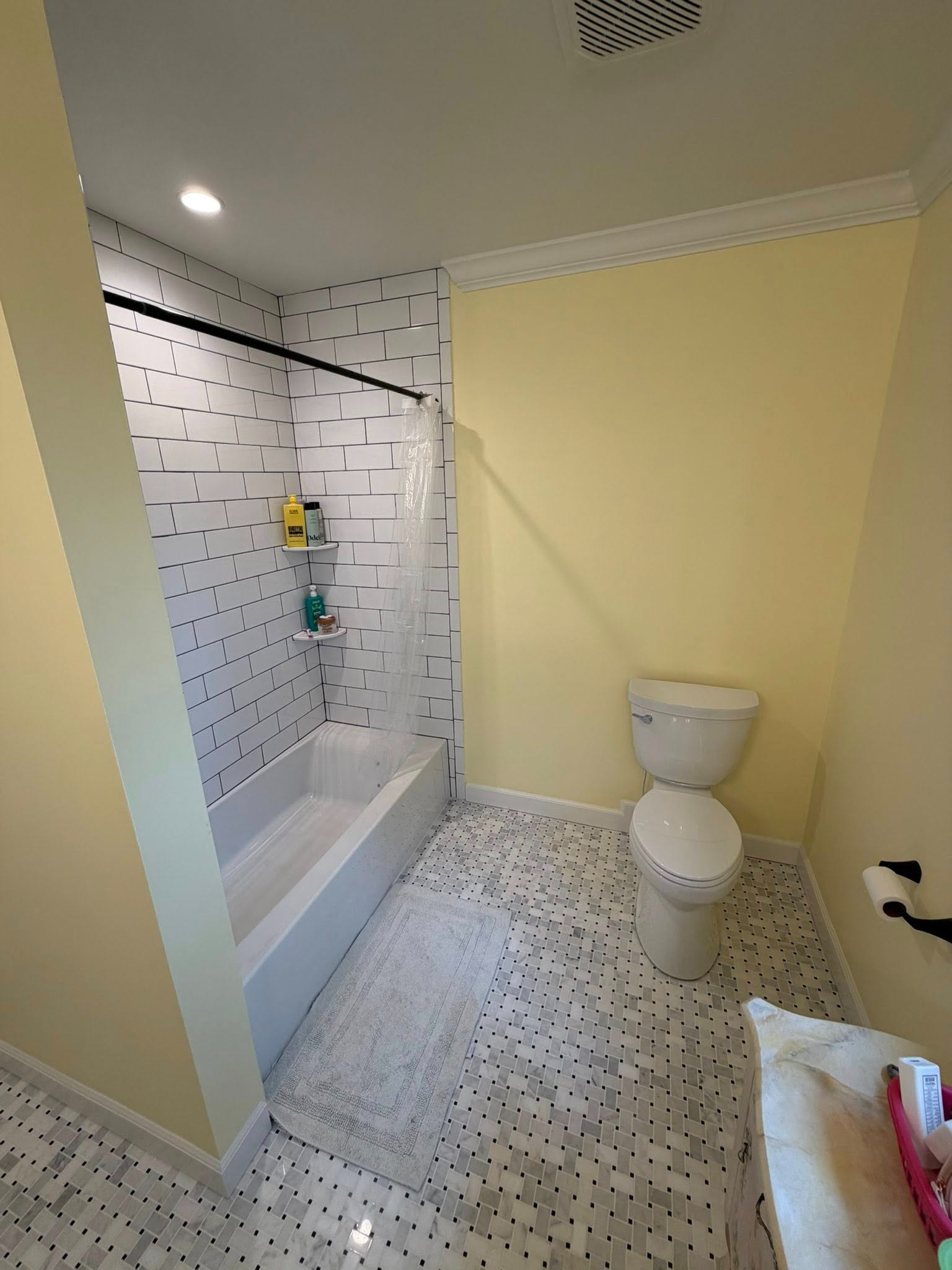 Small bathroom with shower, yellow walls, white tile floor, and a toilet.