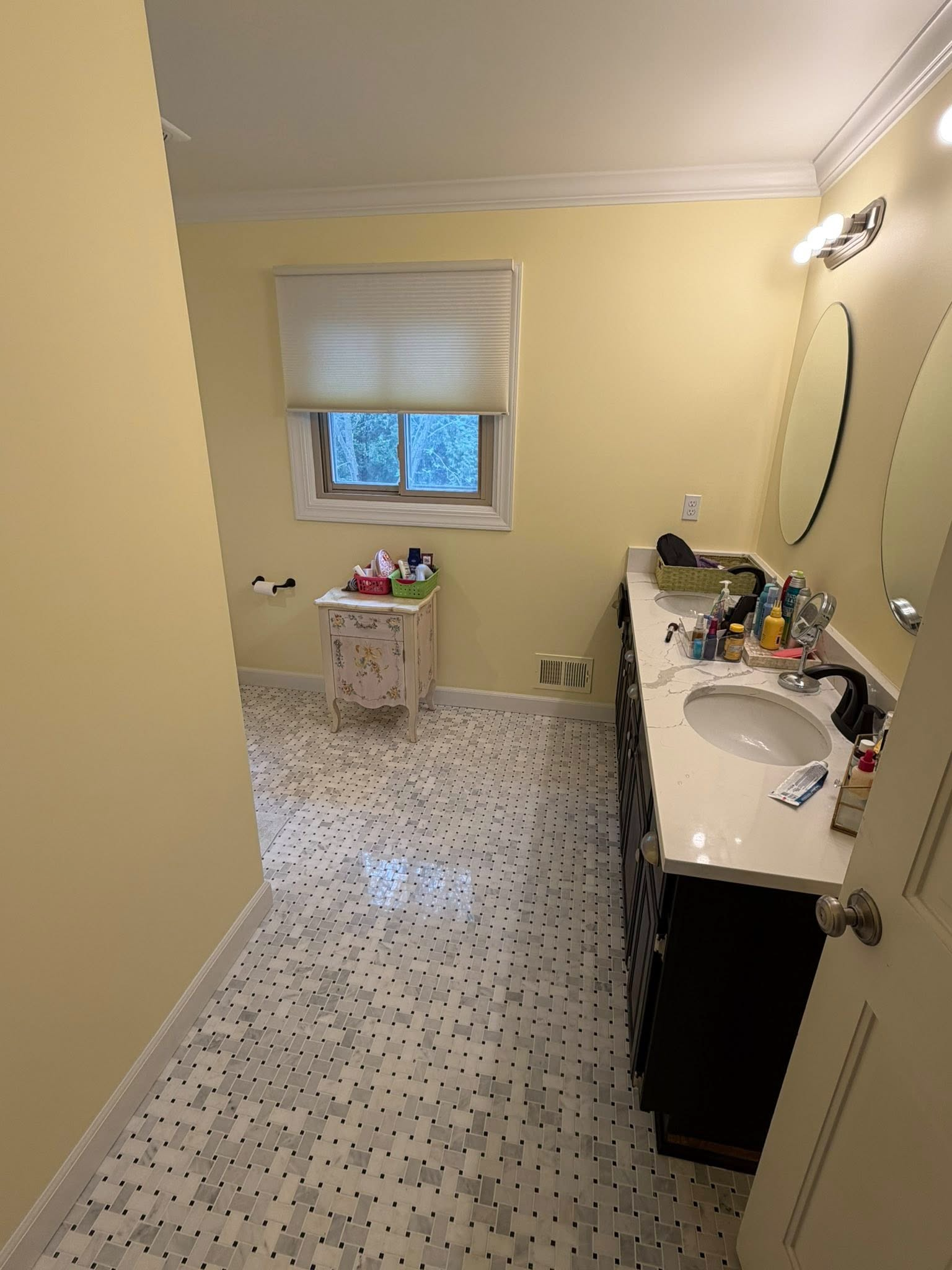 Small bathroom with yellow walls, mosaic tile floor, vanity sink, mirror, and window with blind.