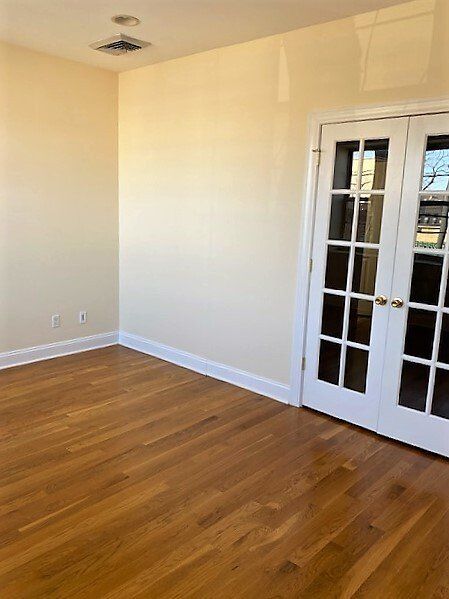 An empty room with pale yellow walls, warm hardwood floors, white baseboards, and a pair of white French doors.