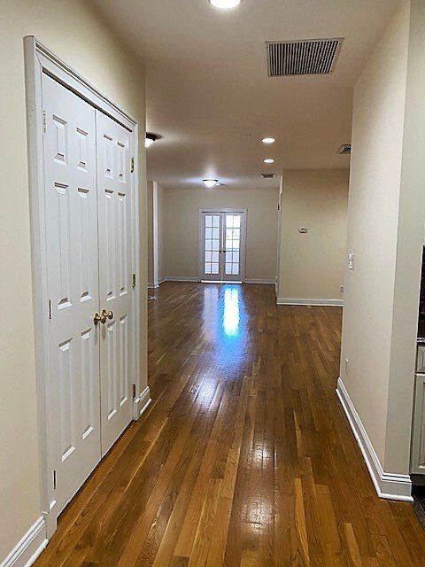 A bright hallway with hardwood floors leads to a room with glass French doors, featuring a white door on the left.