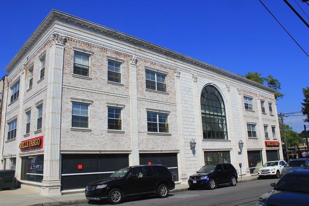 A white, three-story building with a large arched window and ground-floor storefronts on a sunny street with parked cars.