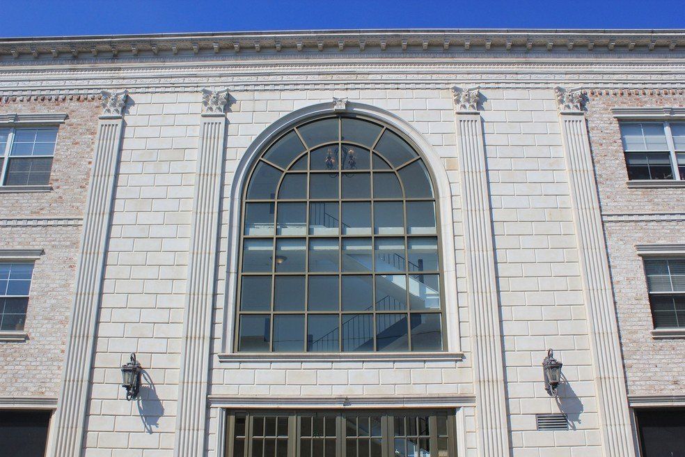 A pale stone facade with two stories, featuring a central arched window flanked by decorative columns and wall lamps.