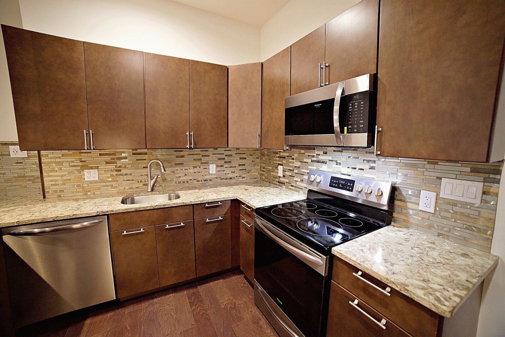 Modern kitchen with dark wood cabinets, granite countertops, stainless steel appliances, and a tiled backsplash.