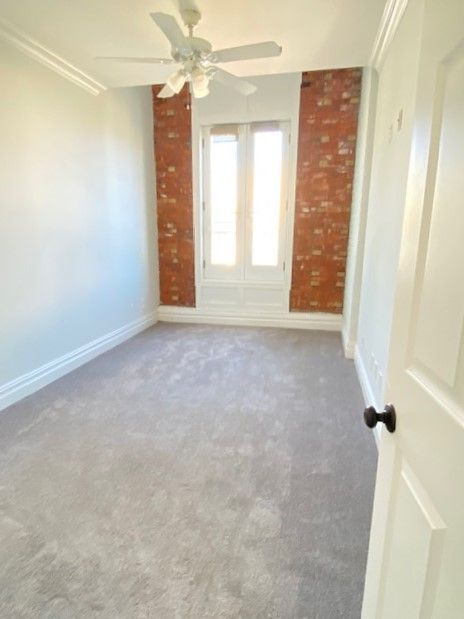 A small, empty room with grey carpet, white walls, a ceiling fan, and two brick accent pillars framing a glass door.