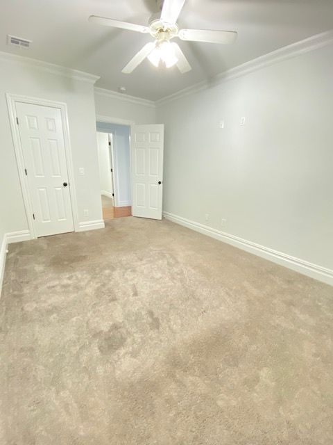 A bright, empty bedroom with light-colored walls, beige carpeting, a white ceiling fan, and two white interior doors.