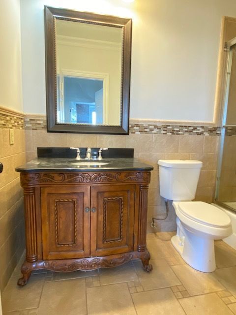A bathroom vanity with a dark countertop and carved wood cabinet next to a white toilet, set against beige tiled walls.