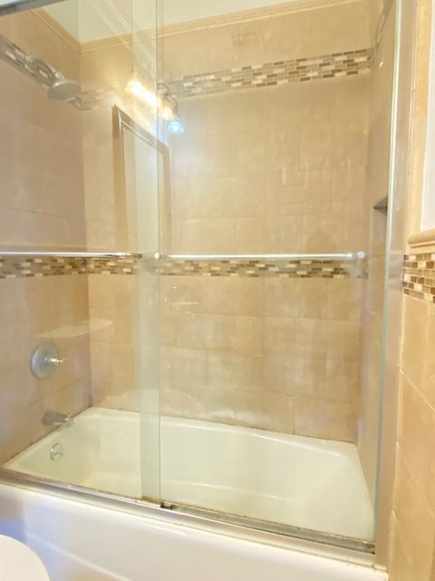 A beige tiled bathtub and shower enclosure with a sliding glass door and decorative horizontal accent tile trim.