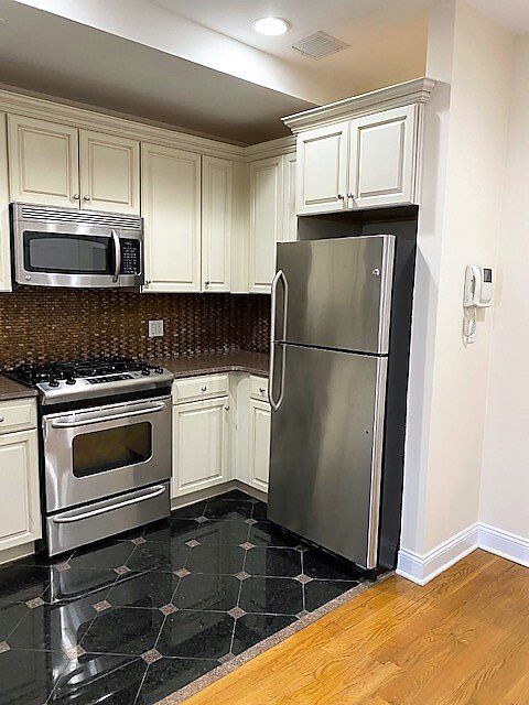 A kitchen featuring off-white cabinets, stainless steel appliances, and a transition from black tile to wooden flooring.