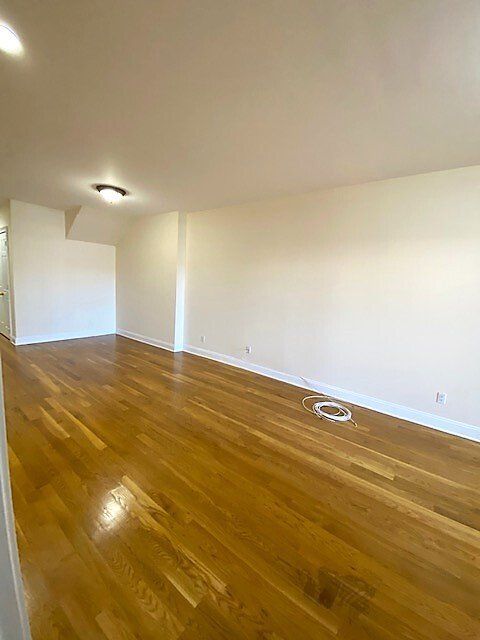 An empty, rectangular room with light hardwood floors, plain white walls, and a recessed ceiling light.