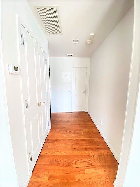 A hallway with light wood flooring, white walls, and white doors leading to rooms at the end and on the left.