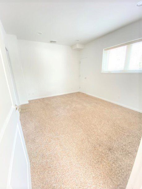Empty white room with beige carpet and a small window on the right.