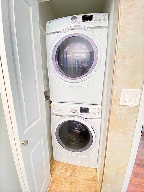 A white stacked washer and dryer unit inside a narrow closet with a light-colored door.