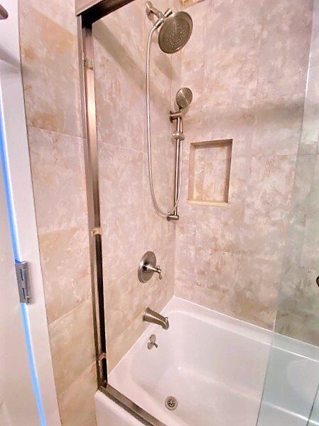 A bathroom shower and bathtub combo with light beige tiled walls, a silver shower head, and a sliding glass door.