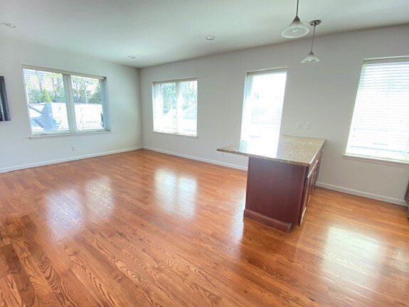 An open-plan room with polished hardwood floors, large windows, and a dark wooden kitchen island under pendant lights.