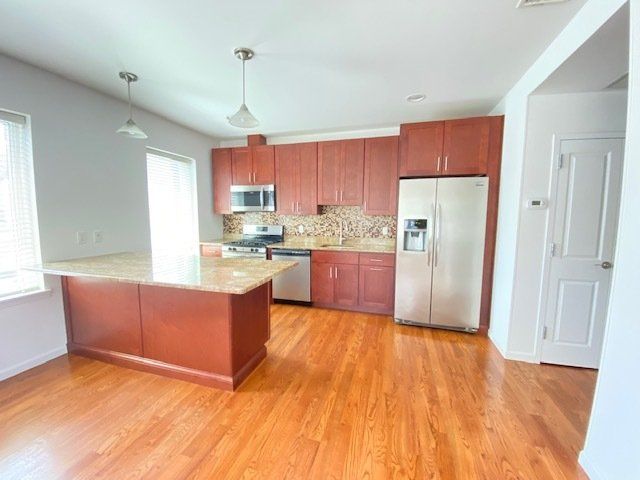 A modern kitchen with cherry wood cabinets, stainless steel appliances, a stone countertop island, and hardwood floors.