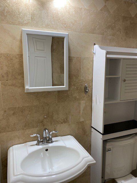 A bathroom vanity with a white sink and faucet, a wall-mounted mirror, and a white storage unit positioned over the toilet.