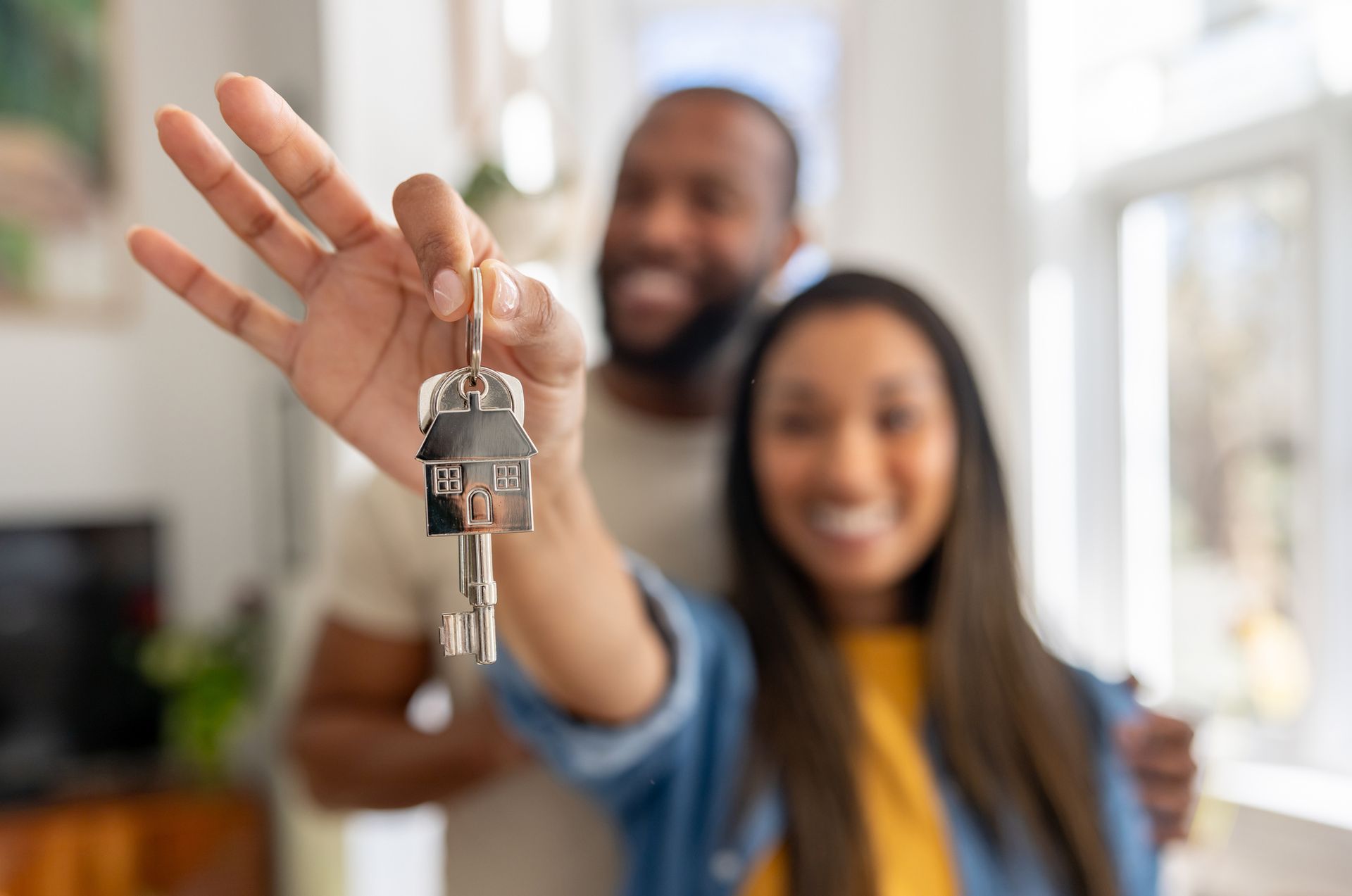 Hand holding house-shaped keychain with keys indoors