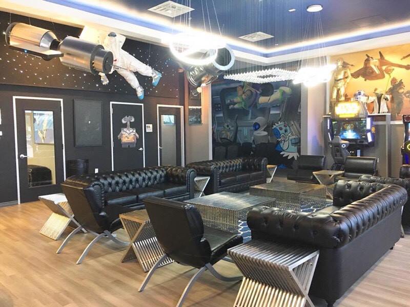 Modern lounge with black leather sofas, metal chairs, mirrored walls, and decorative ceiling art