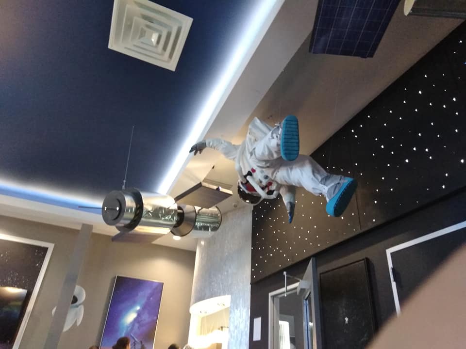 Person in a Spider-Man suit hanging upside down in a modern room with starry wall decor.