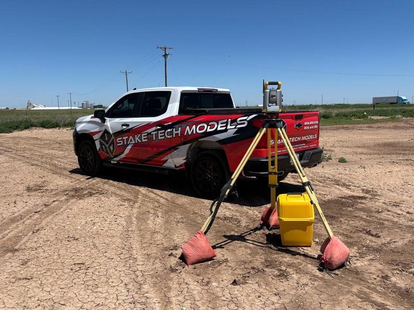 Survey truck with tripod-mounted survey equipment in a dirt field under a clear blue sky