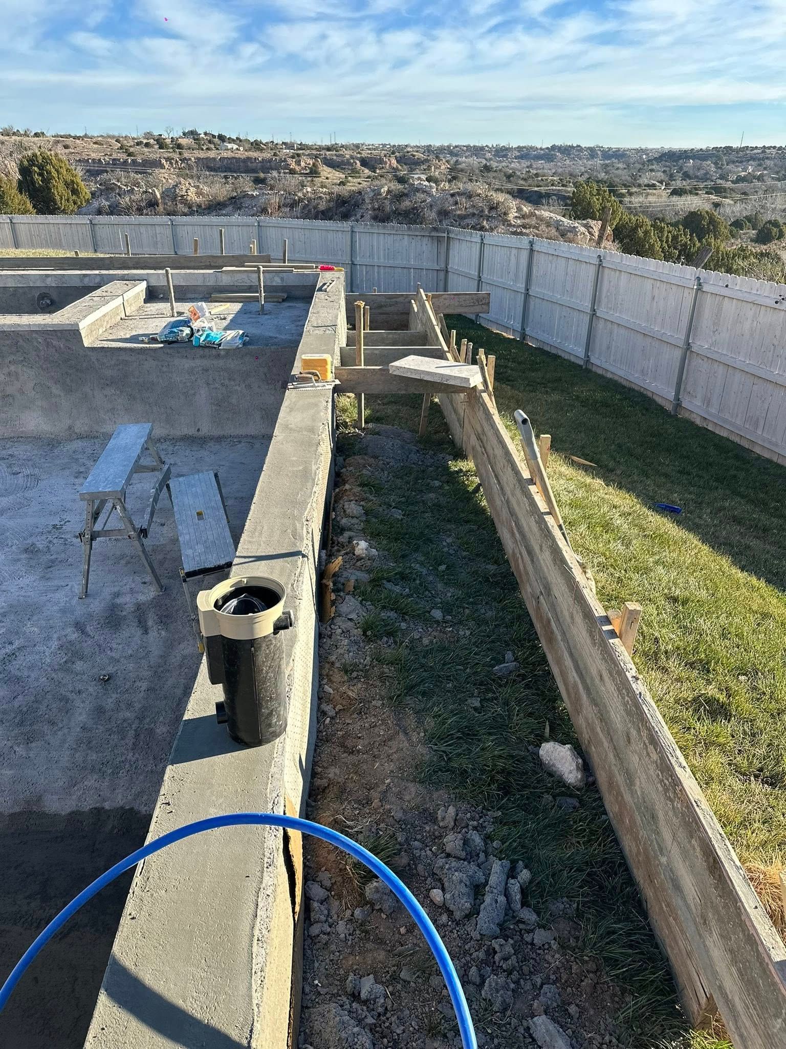 Backyard with concrete retaining walls, gravel, grass, and a blue hose in the foreground