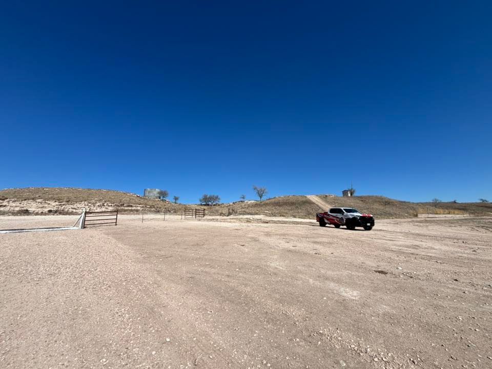 Dark SUV parked on a sandy desert lot under a clear blue sky with low hills in the background