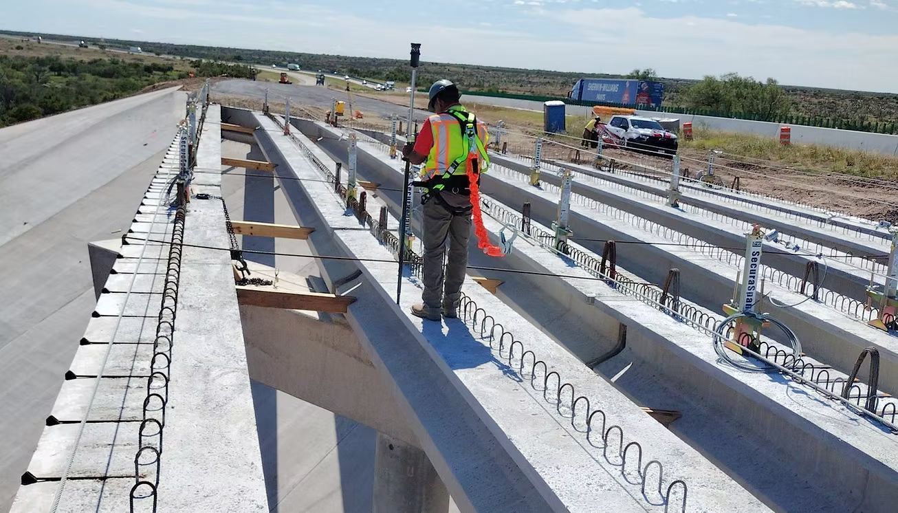 Construction worker in a neon vest standing on concrete bridge beams at a highway site