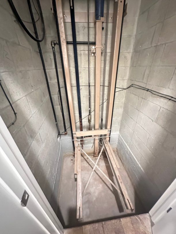 Wooden clothes drying rack in a small, windowless concrete-walled room, surrounded by pipes.