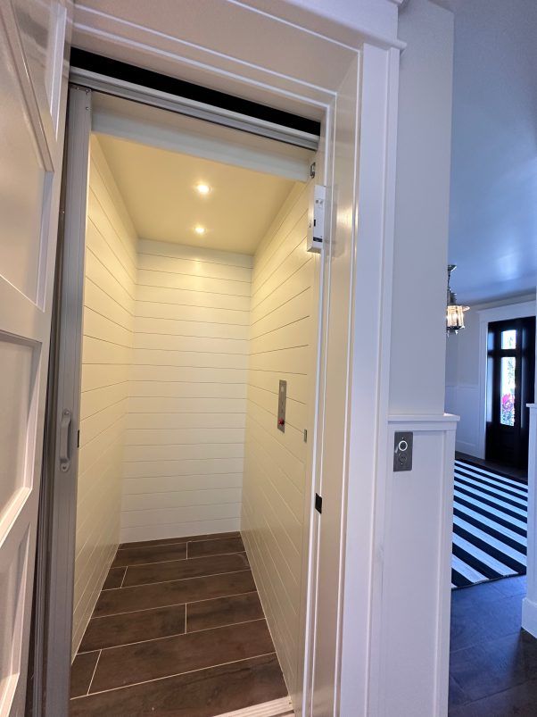 Elevator interior with white paneled walls, recessed lighting, and a dark tile floor.