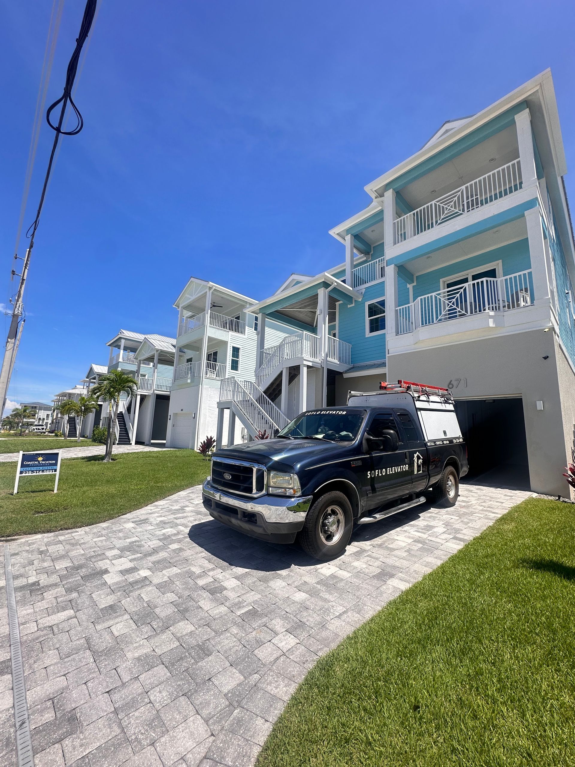 Blue and white beach houses with a black pickup truck in the driveway under a bright blue sky.