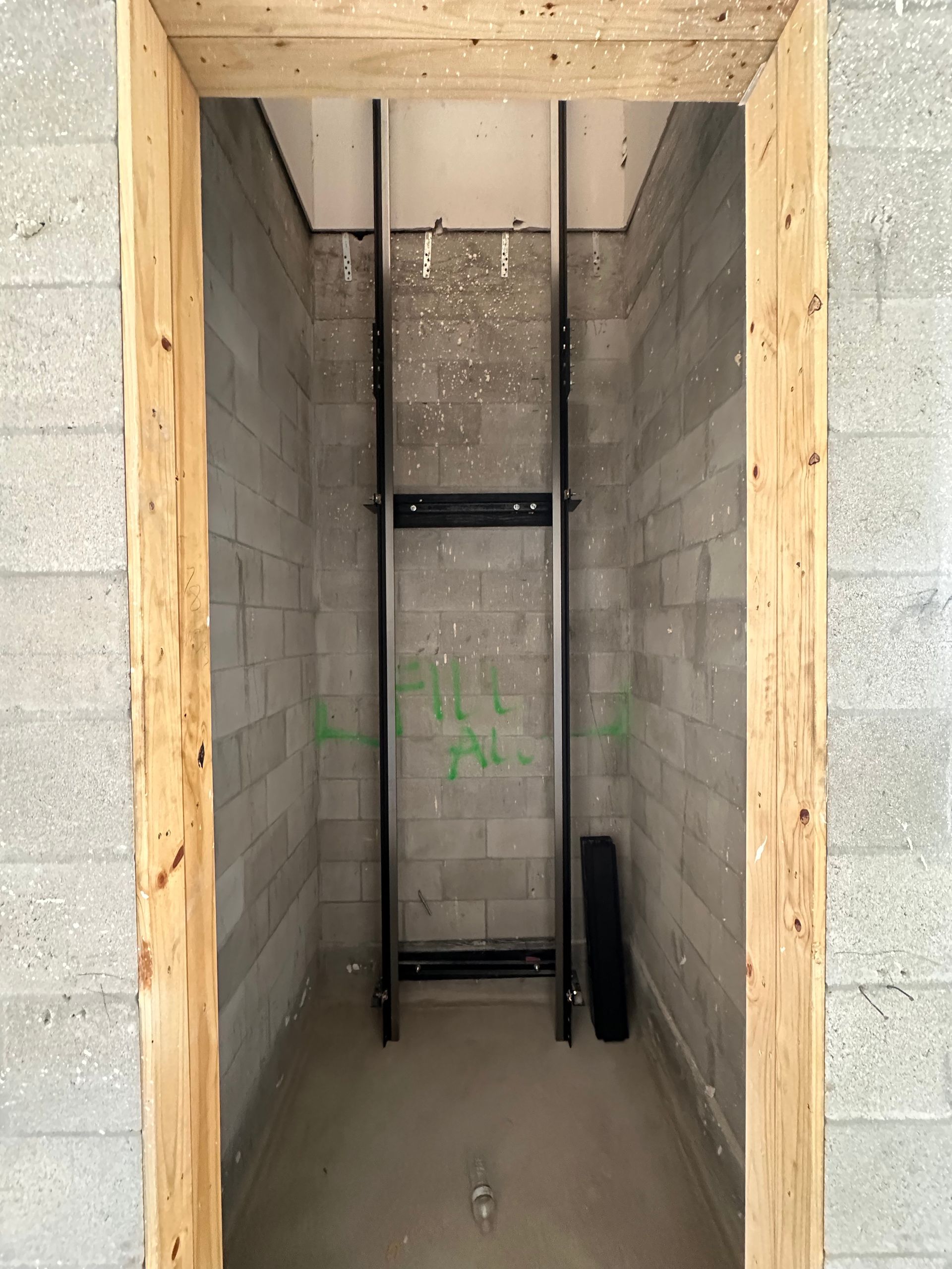 Construction site interior with a metal lift track in a concrete block shaft, framed by wooden beams.