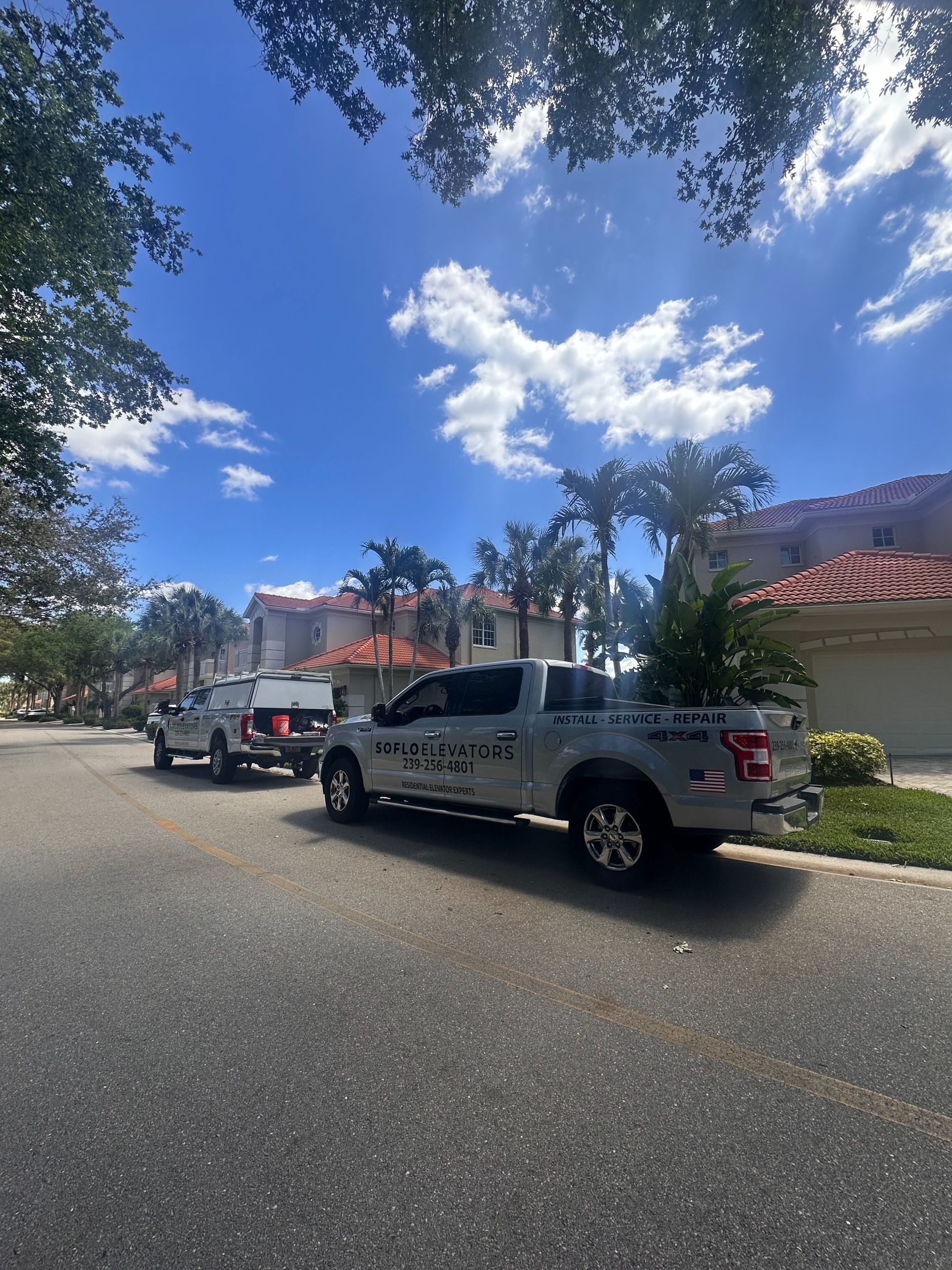 Street view of parked pickup trucks under a bright blue sky with trees and houses nearby