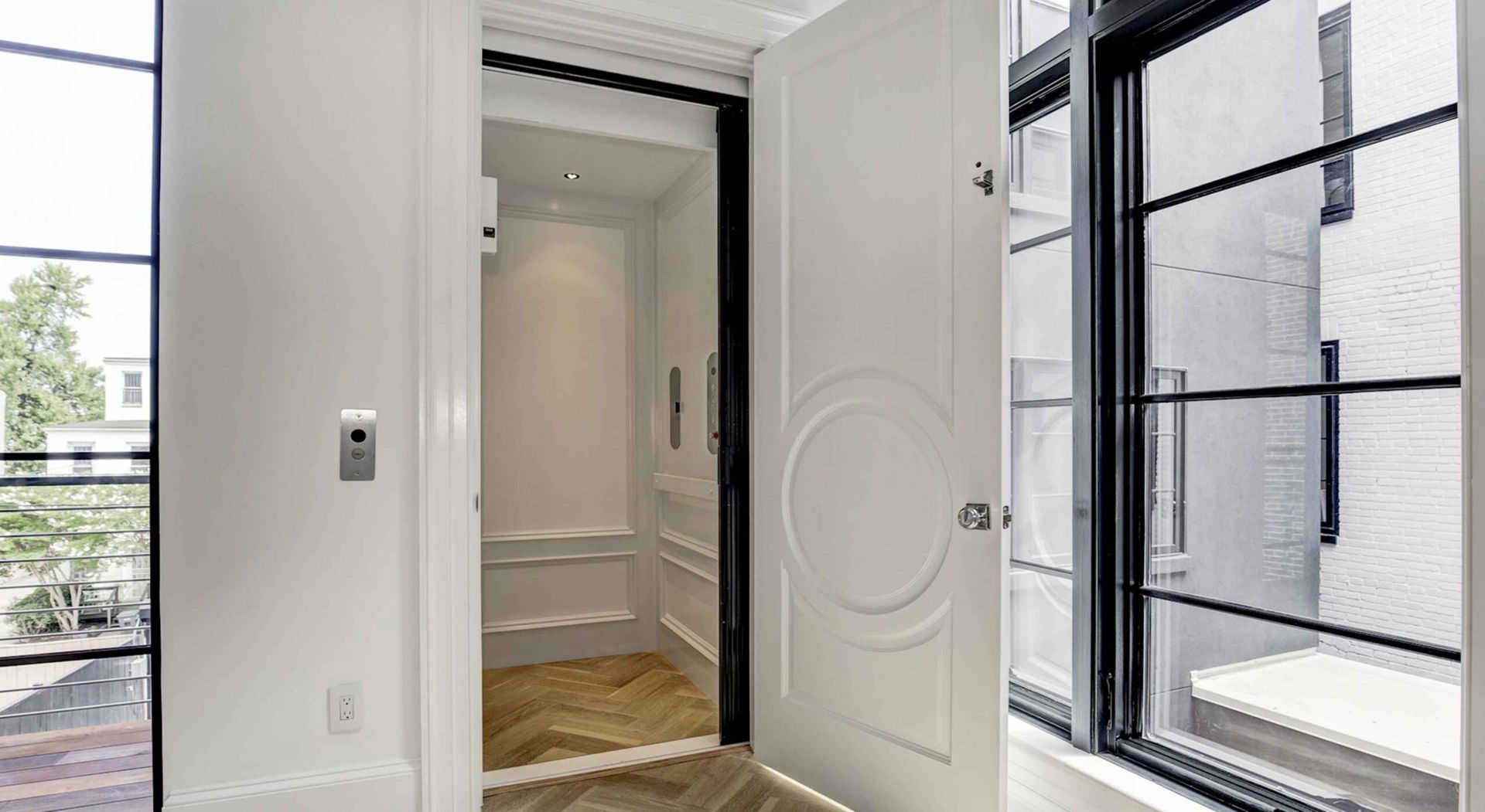 Interior view: Elevator with open white door, black-framed windows, white walls.