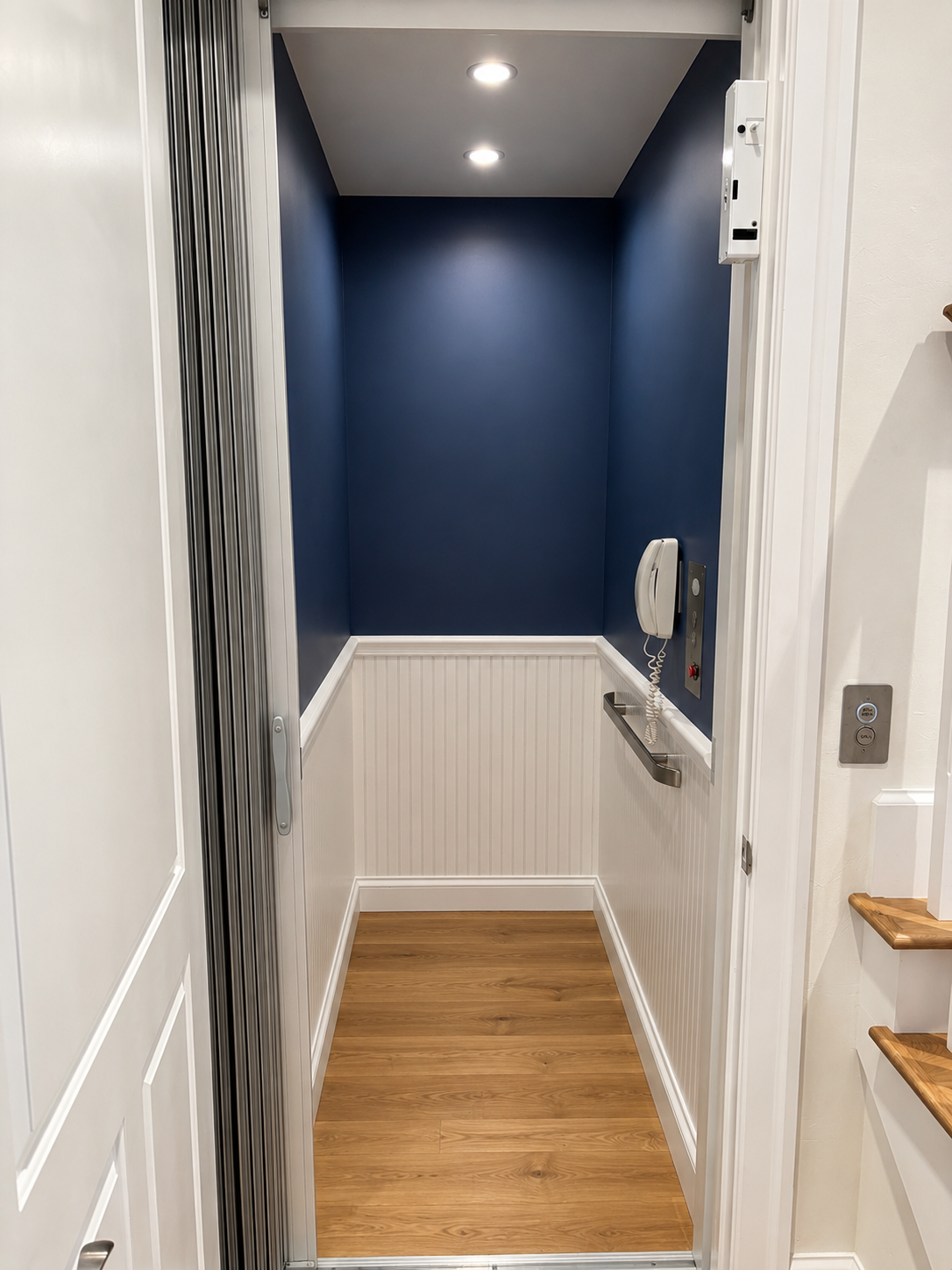 Narrow hallway with blue accent wall, white wainscoting, wood floor, and recessed ceiling lights