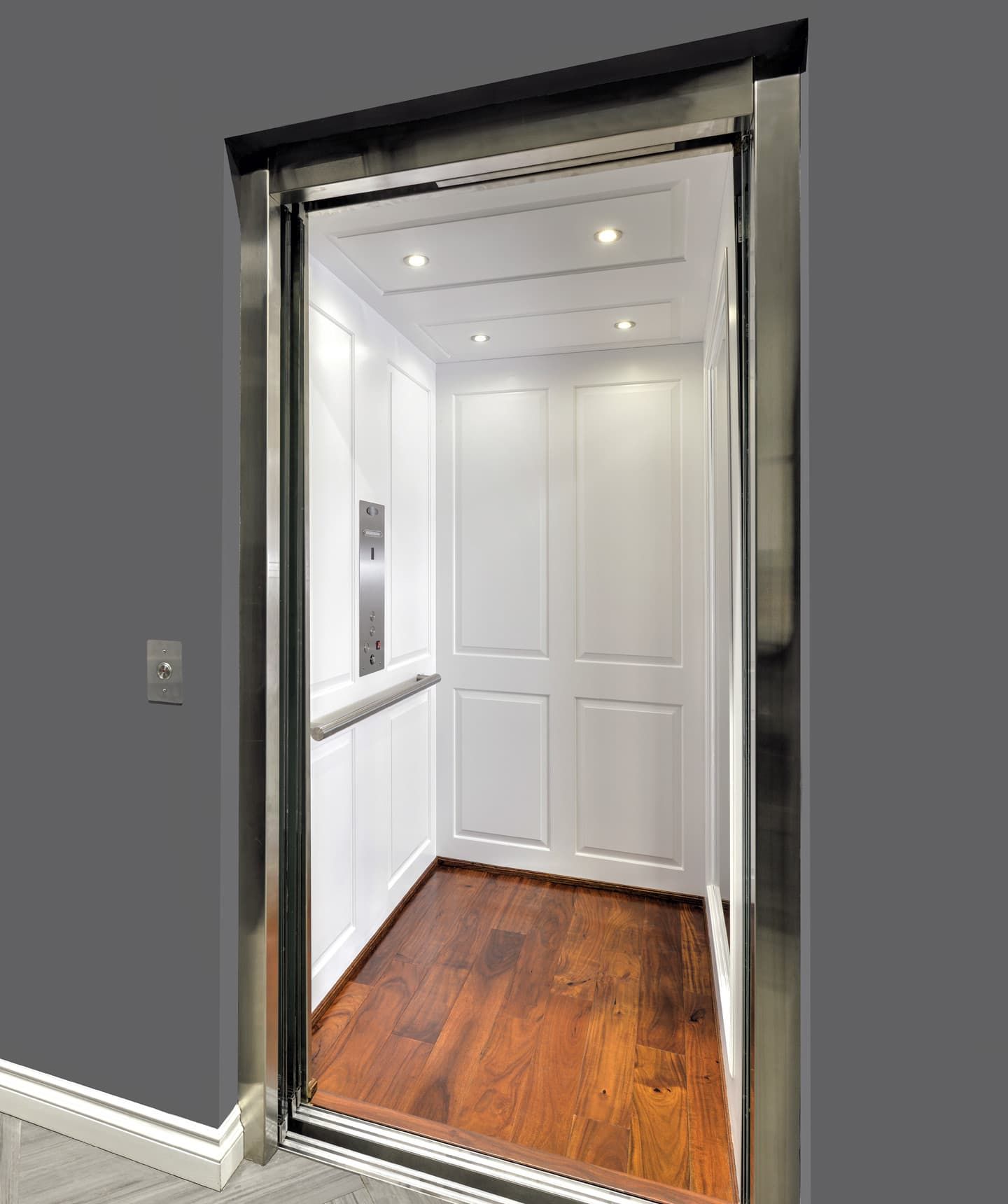 Elevator interior with white paneled walls, wood floor, chrome accents, and call button.