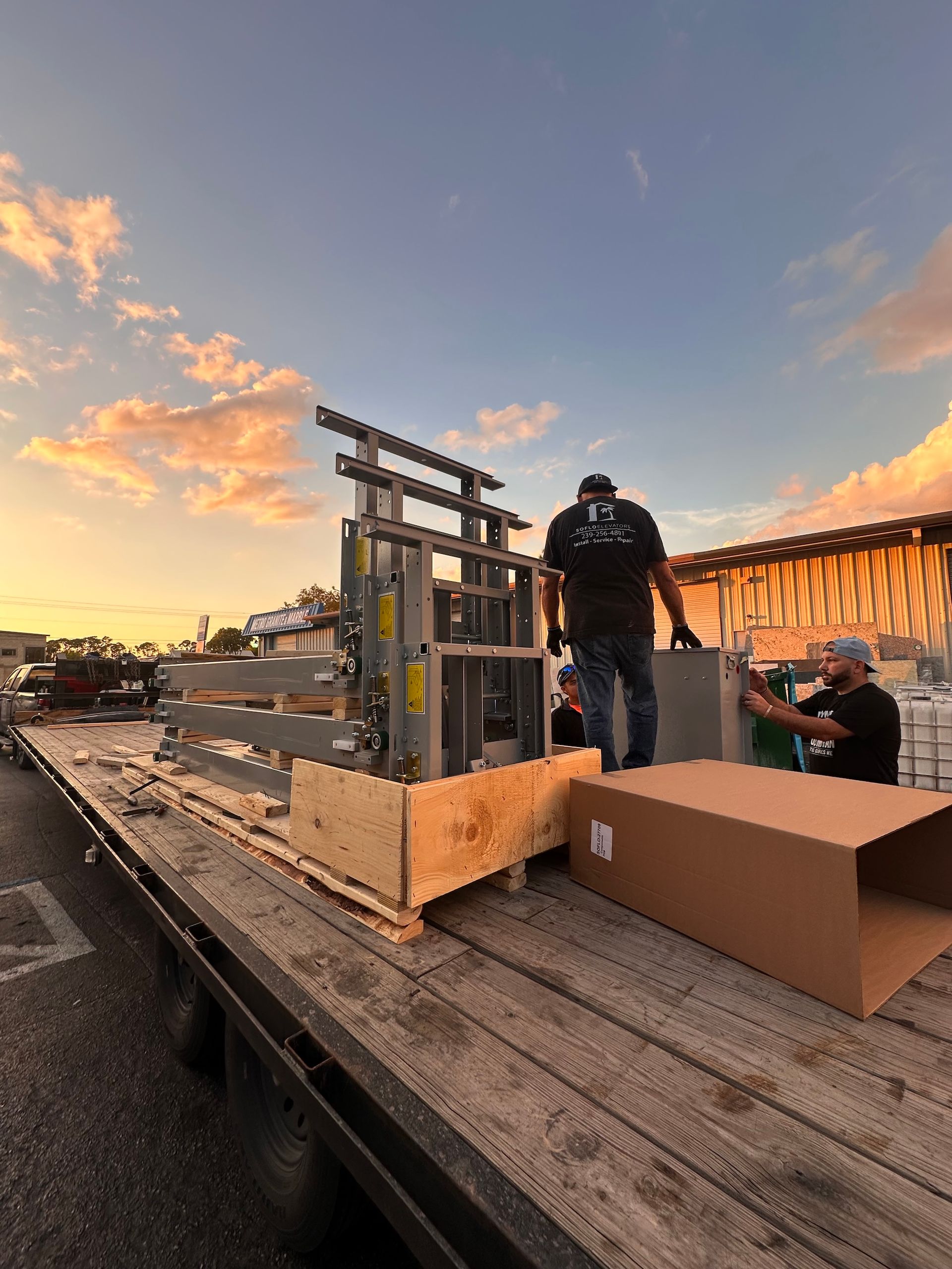 Workers unloading equipment from a flatbed truck at sunset.