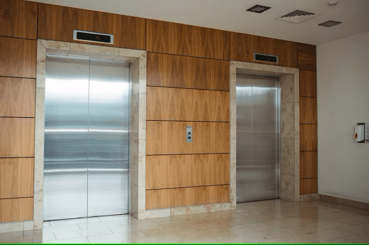 Two stainless steel elevators with closed doors in a wood-paneled hallway.