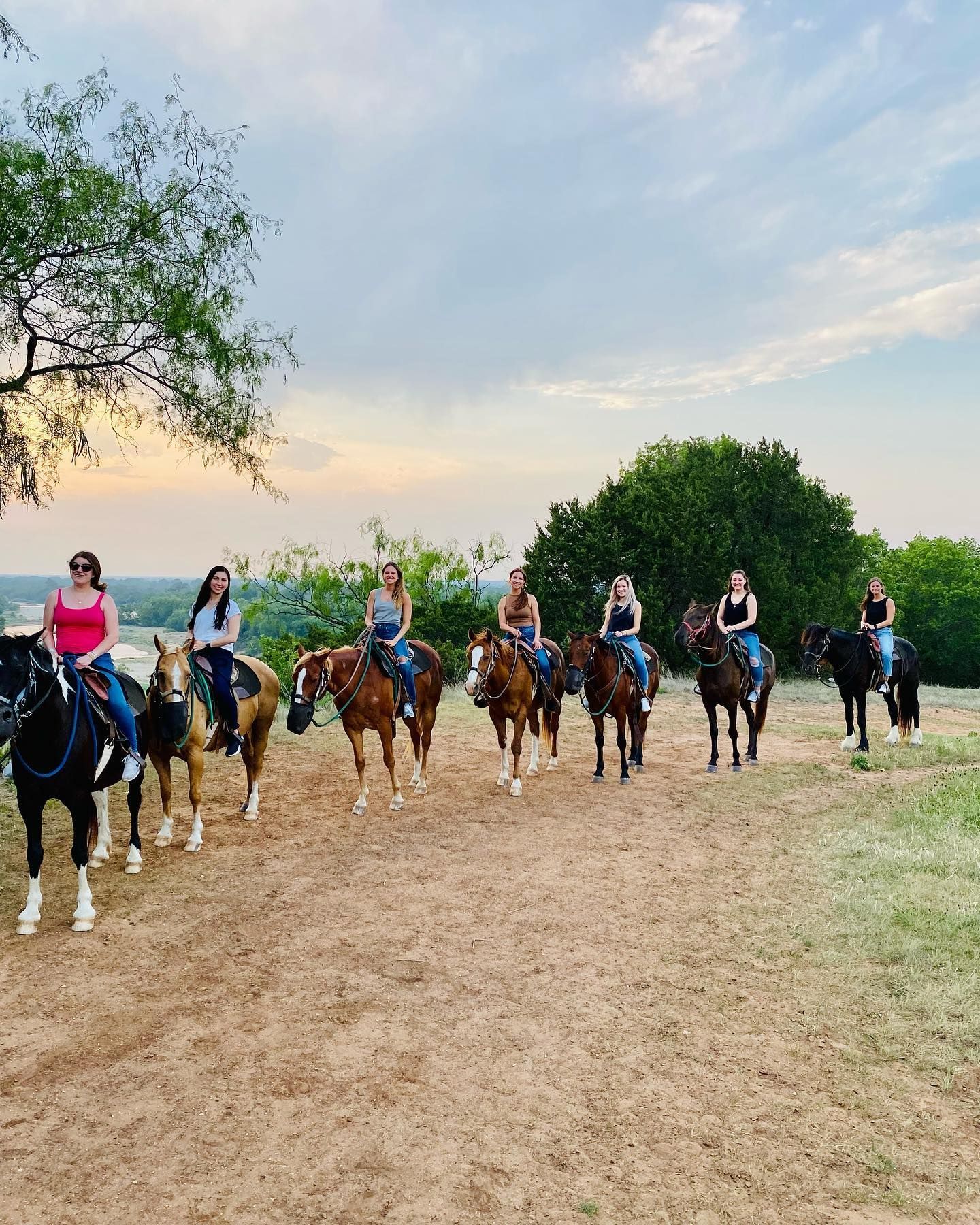 Group of people horseback riding outdoors at dusk.