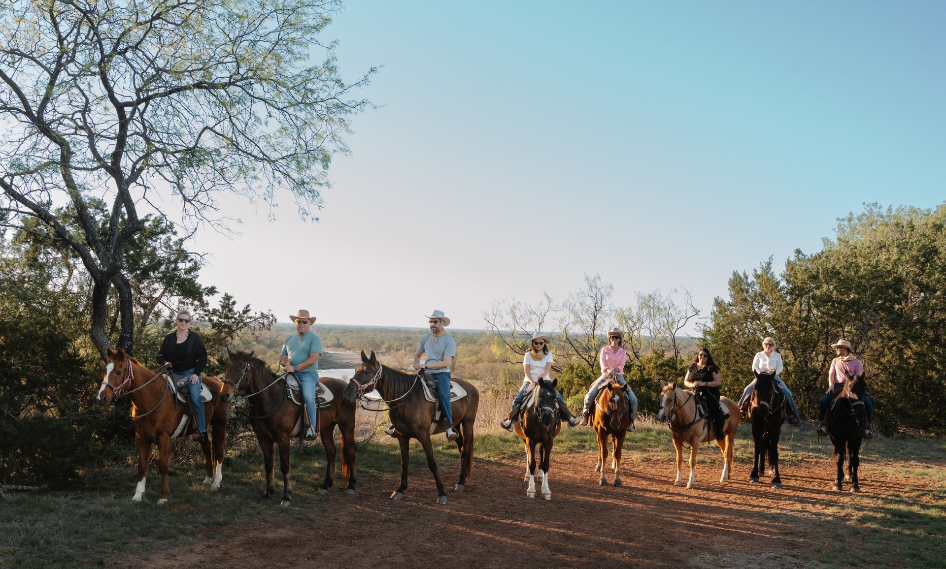 Cowboys on horseback lined up in a dusty field under a clear sky, holding lasso ropes.