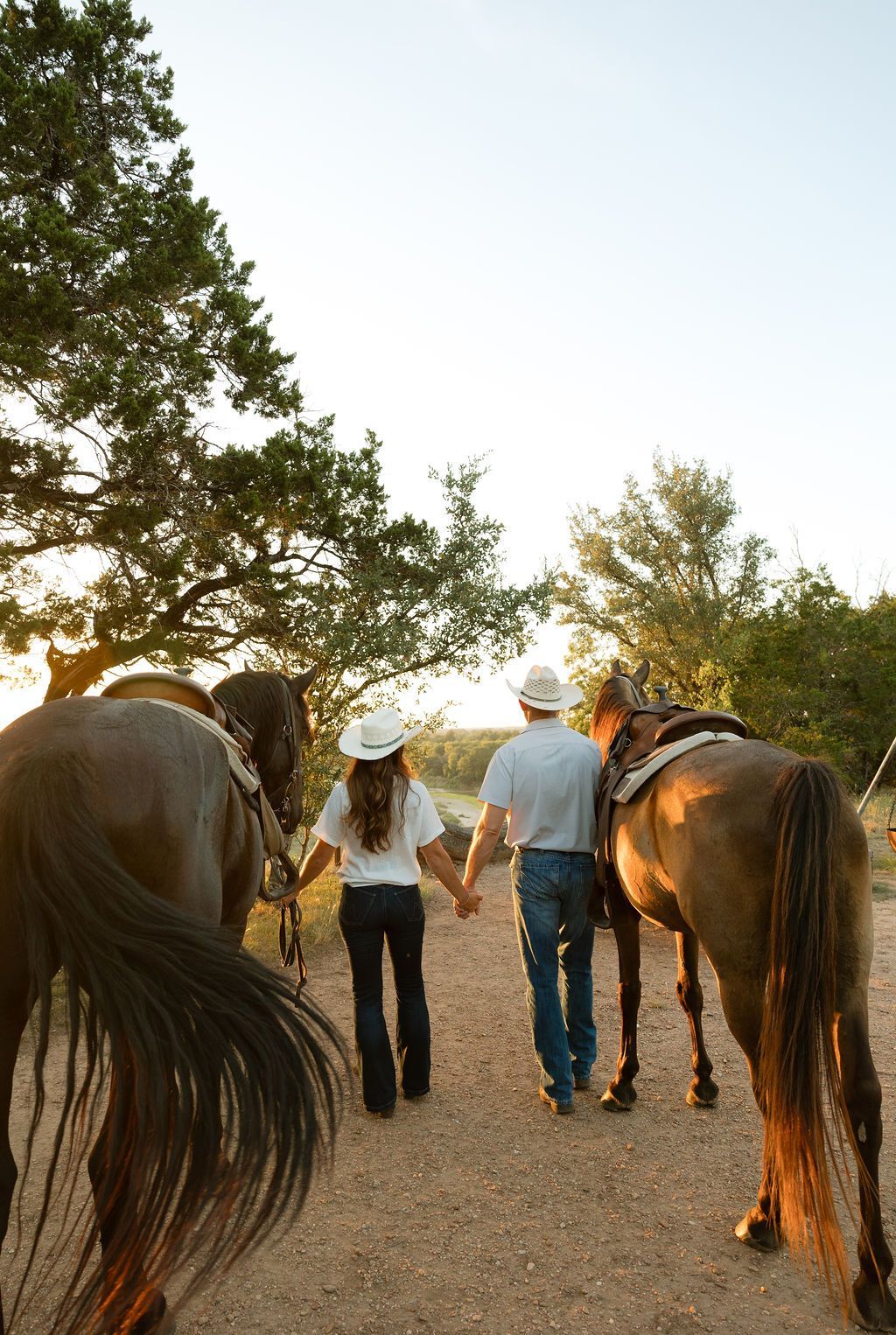 Sunset scene: Three people with horses on a grassy field. One rides, two stand nearby; vibrant sky, flowers in foreground.