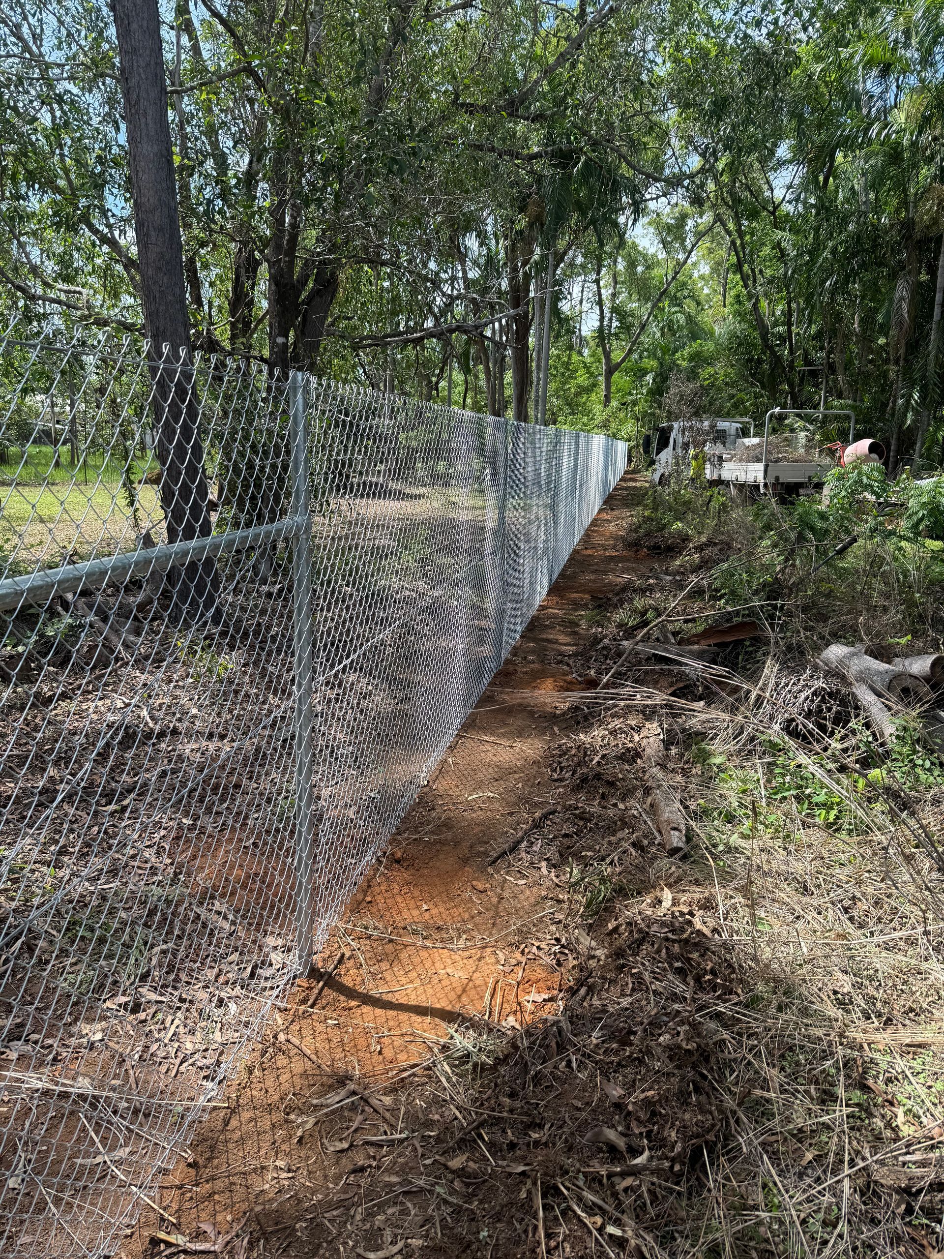 Chain link fence in a wooded area, brown dirt path alongside. — True North Fencing in Noonamah, NT