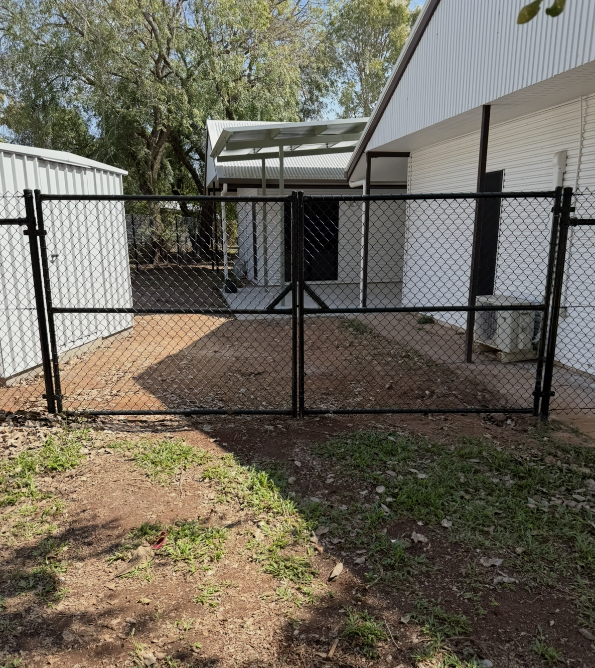 Black chain-link fence with double gate in front of a white building with a covered entryway and a concrete pad. — True North Fencing in Noonamah, NT