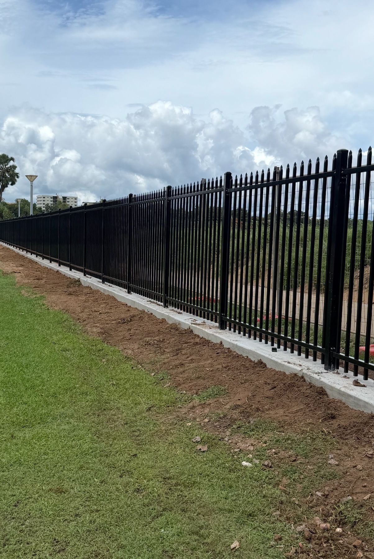 Black fence bordering grass and a cloudy sky. — True North Fencing in Noonamah, NT