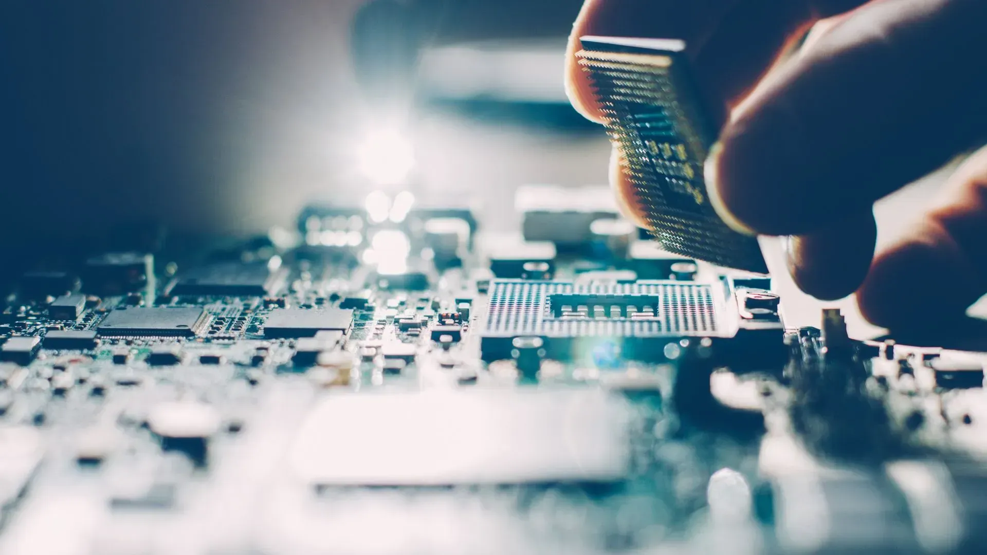 Primer plano de una mano colocando un componente electrónico en una placa de circuito impreso bajo una luz intensa