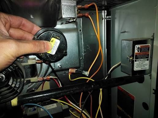Hand holding a small black HVAC blower motor inside a metal appliance cabinet with orange wires.