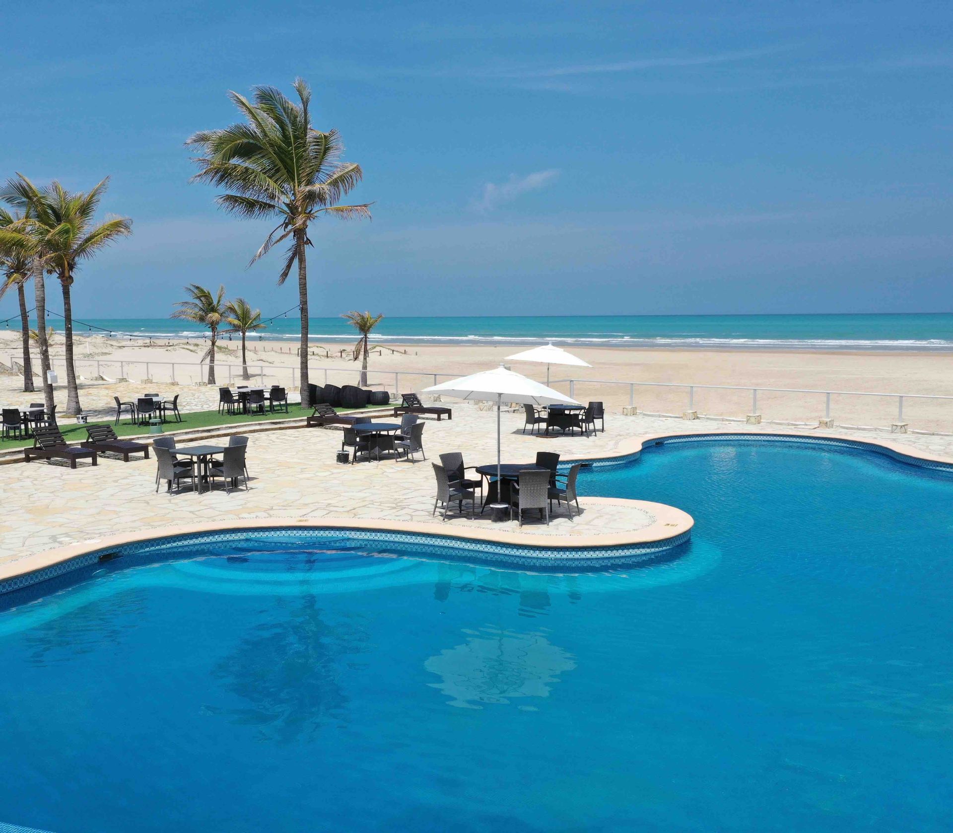 A large swimming pool surrounded by tables and chairs on a beach.