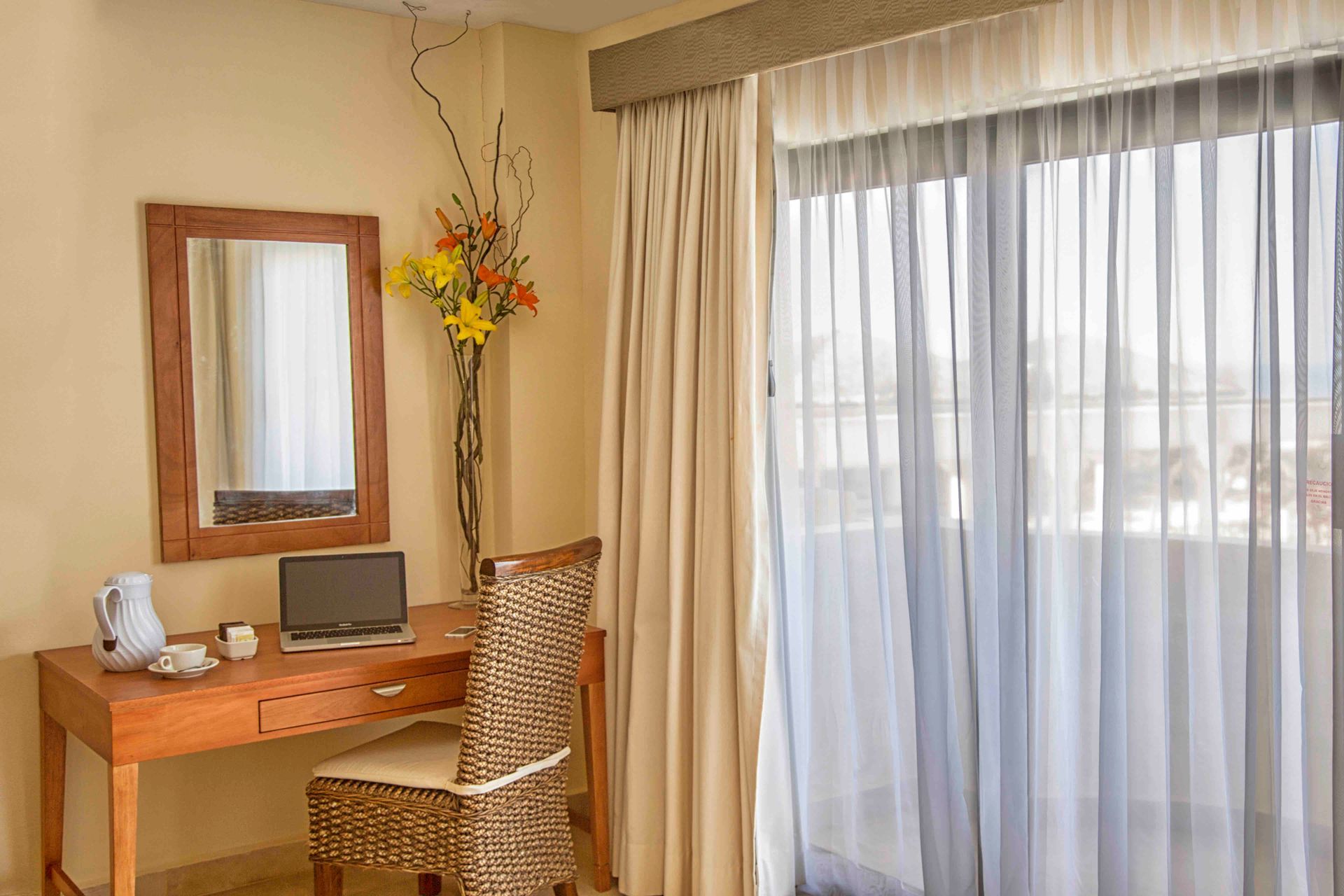 A hotel room with a desk , chair , mirror and sliding glass doors.