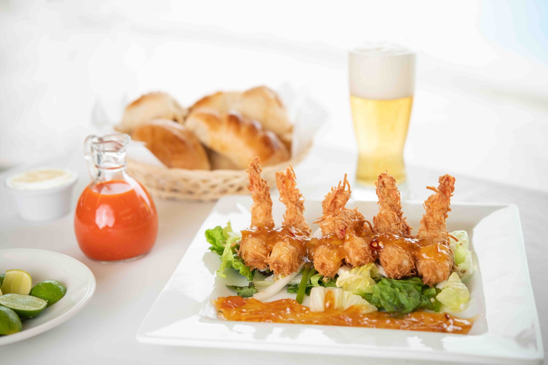 A white plate topped with fried shrimp and lettuce next to a glass of beer and a basket of bread.