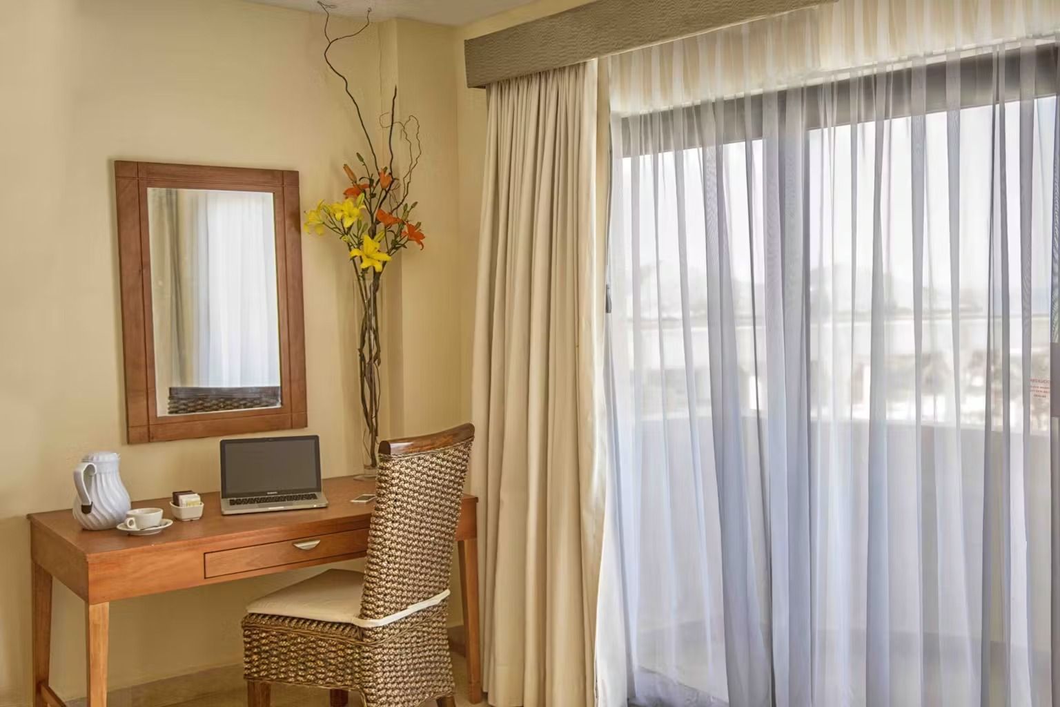 A hotel room with a desk , chair , mirror and sliding glass doors.